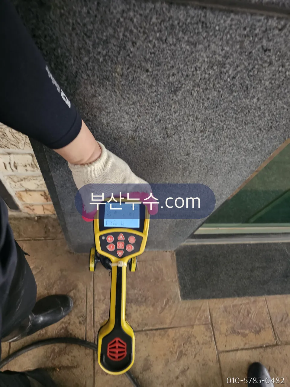 휴대 탐지기로 벽면 누수 신호를 확인하는 장면